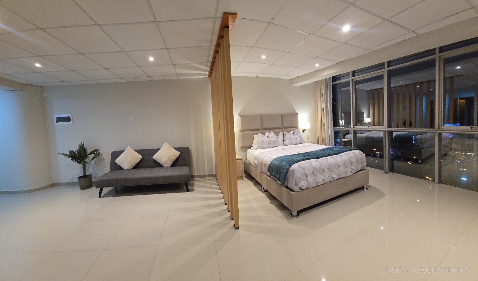 SUMAQ SUITE queen bed and sofa illuminated at night beside panoramic windows